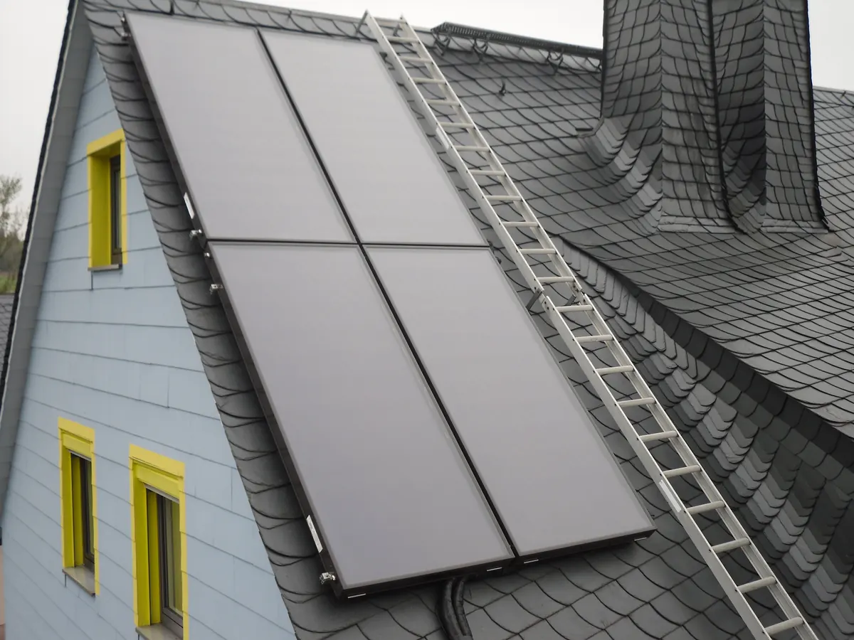 Quatro coletores de aquecedor solar lado a lado num telhado inclinado (foto ilustrativa)