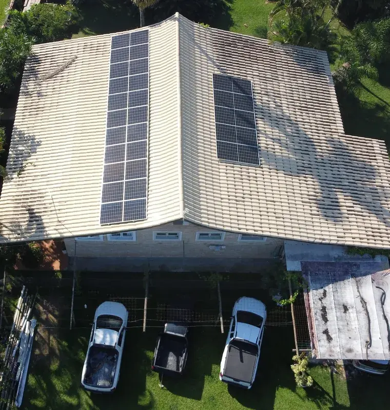 Vista aérea de drone de residência em Caraguatatuba/SP com 16 placas solares em dois grupos no telhado de telhas claras