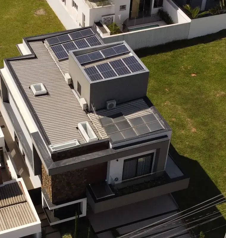 Vista aérea de residência com fachada de pedra em Sorocaba/SP, com módulos fotovoltaicos no volume superior e na cobertura